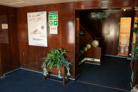 The top of the port-side staircase leading up from the lobby to the cafeteria, showing the public facilities available....